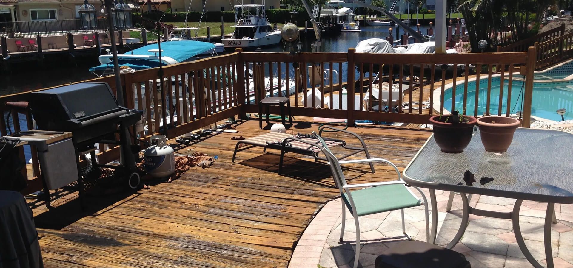 Aged wooden deck with patio furniture and grill overlooking a canal and pool.