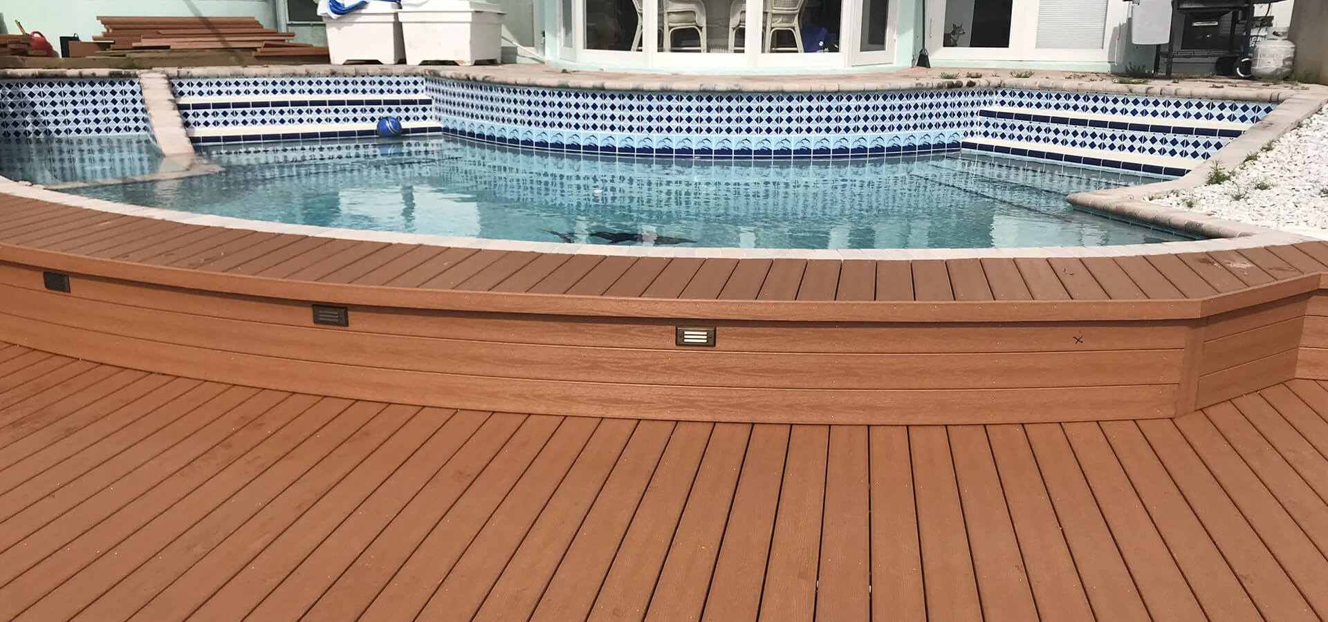 Rich brown composite poolside deck with integrated lighting beside tiled pool.
