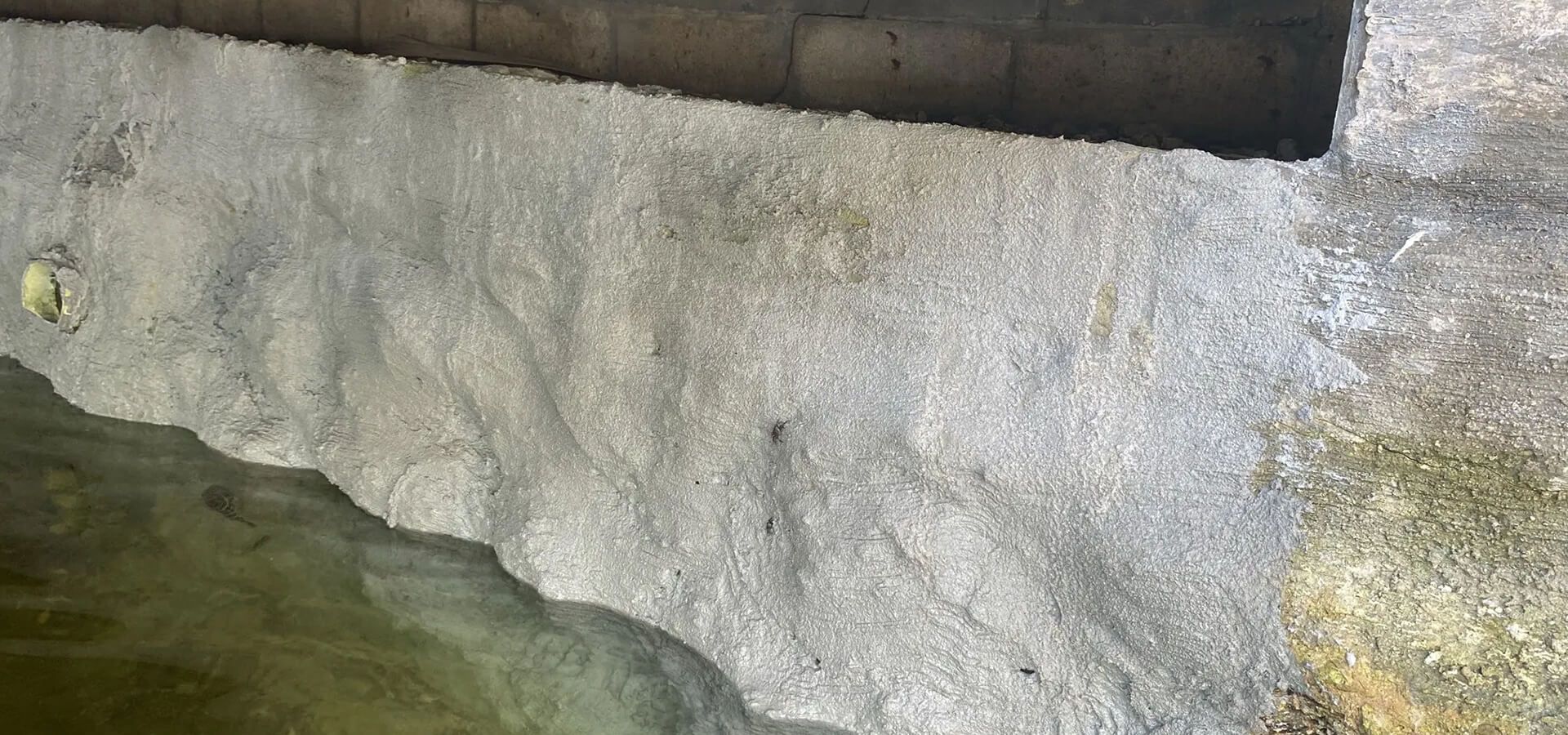 Textured concrete seawall edge partially submerged in water, showing waterline.