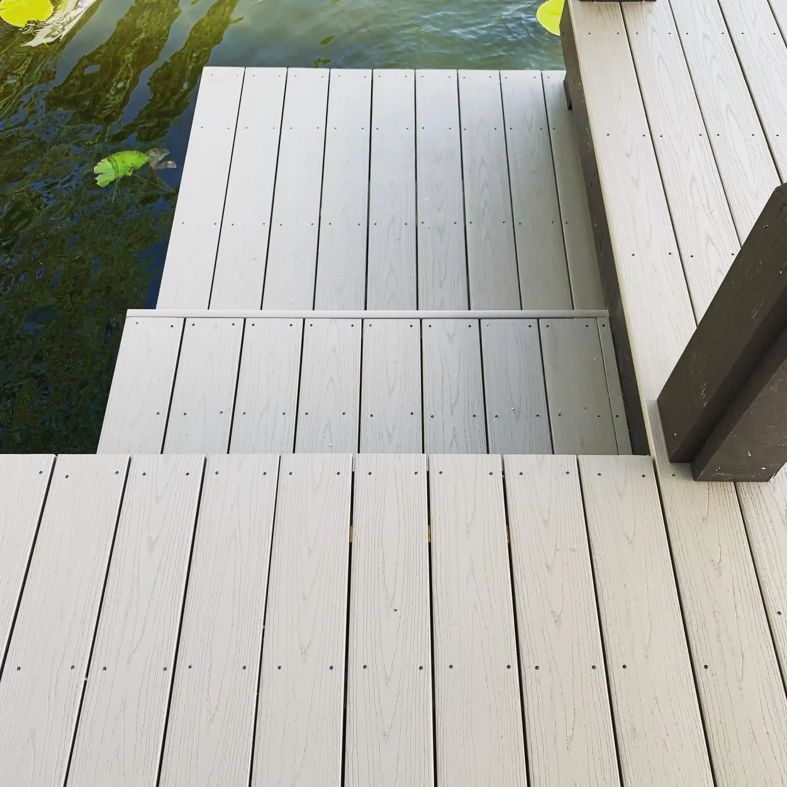 Light-gray dock steps descending to water level next to lily pads.