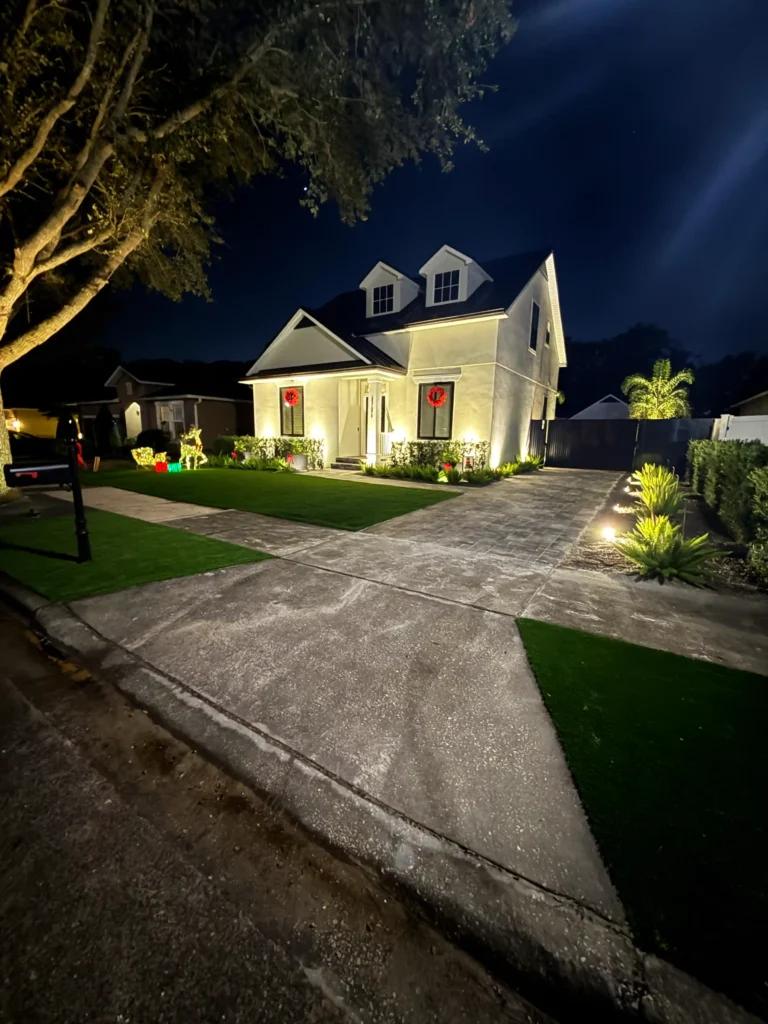 Two-story house with exterior window lights illuminating the facade and front yard at night.