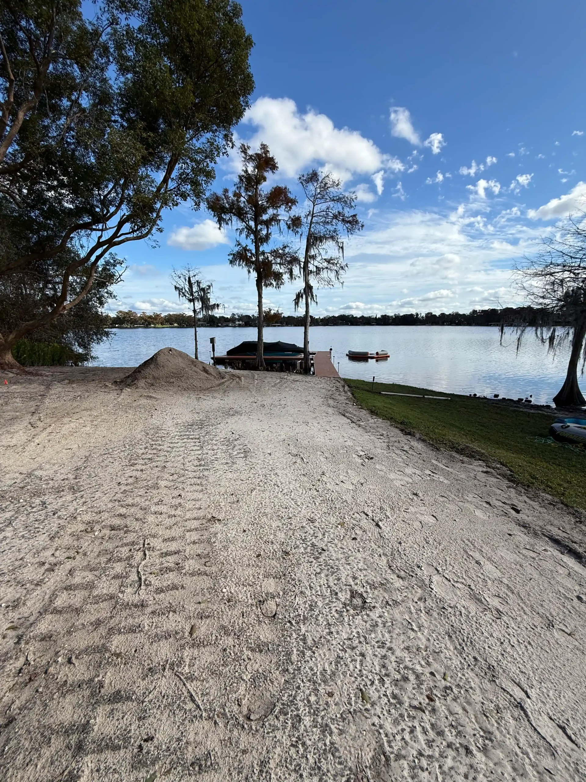 Sandy shoreline with tire tracks leading to a distant dock and boats.