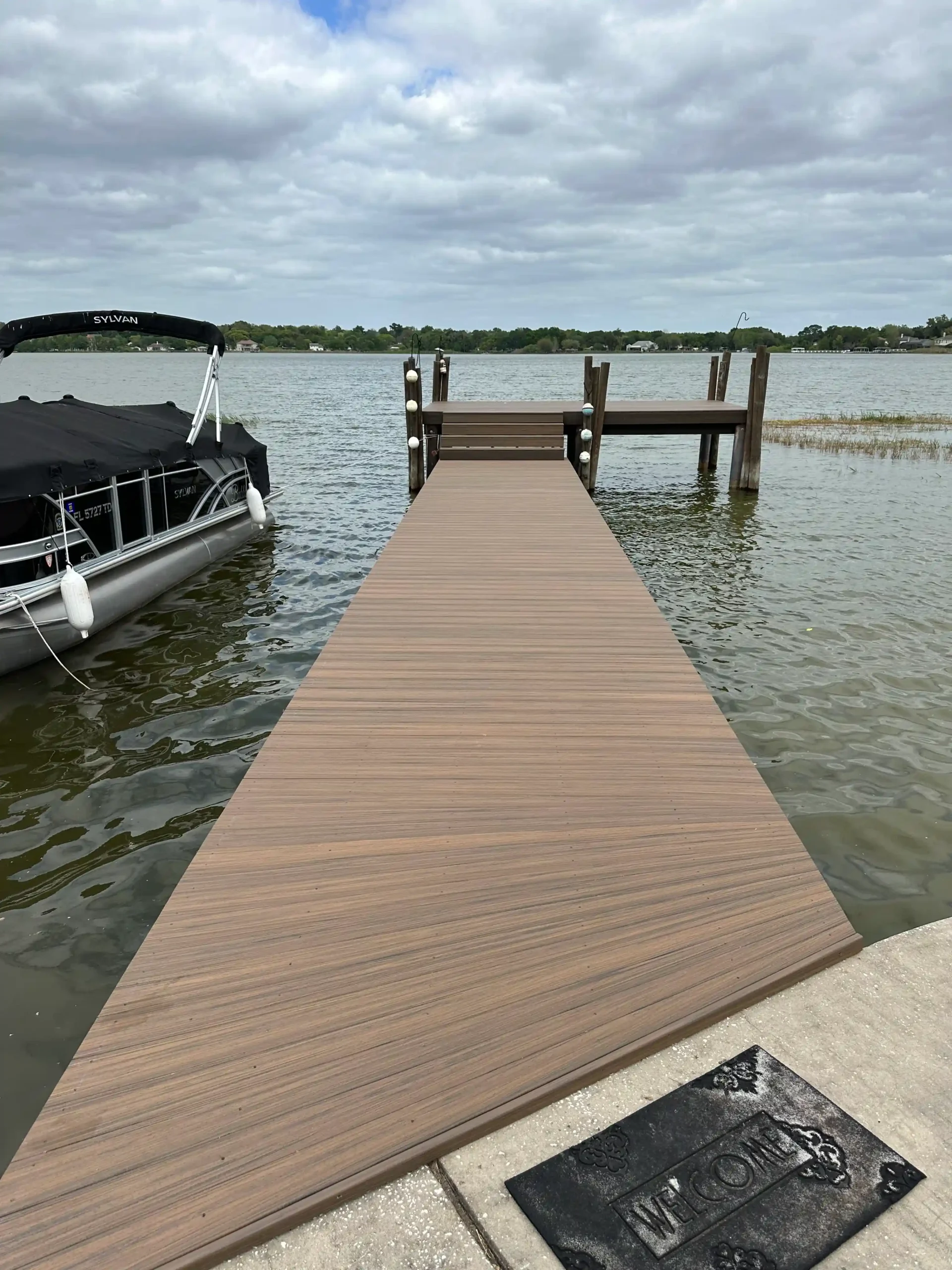 Narrow brown dock leading to a boat slip, set on a slightly rippled lake.