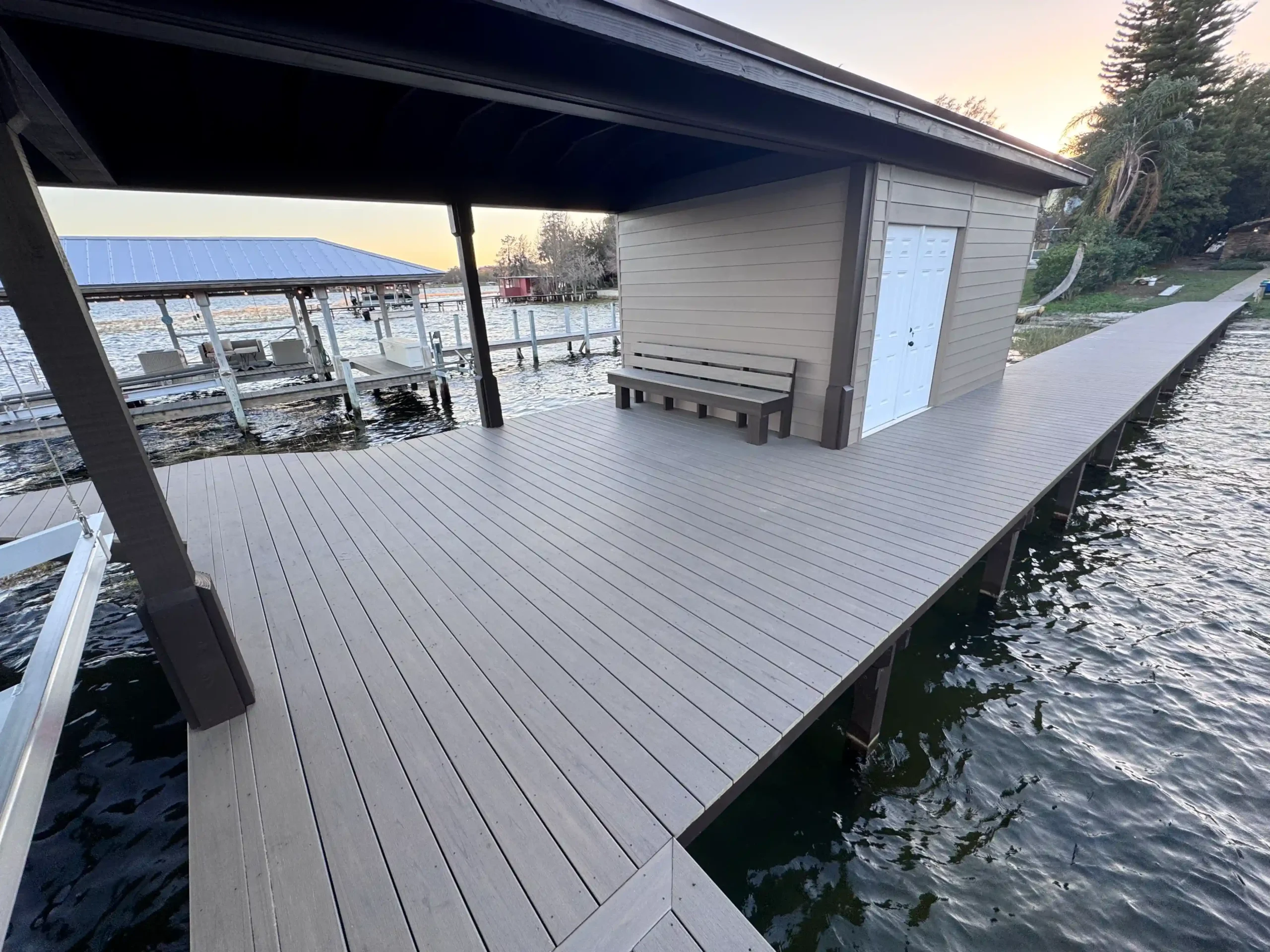 A wide dock with storage shed and bench, stretching along a calm lake.