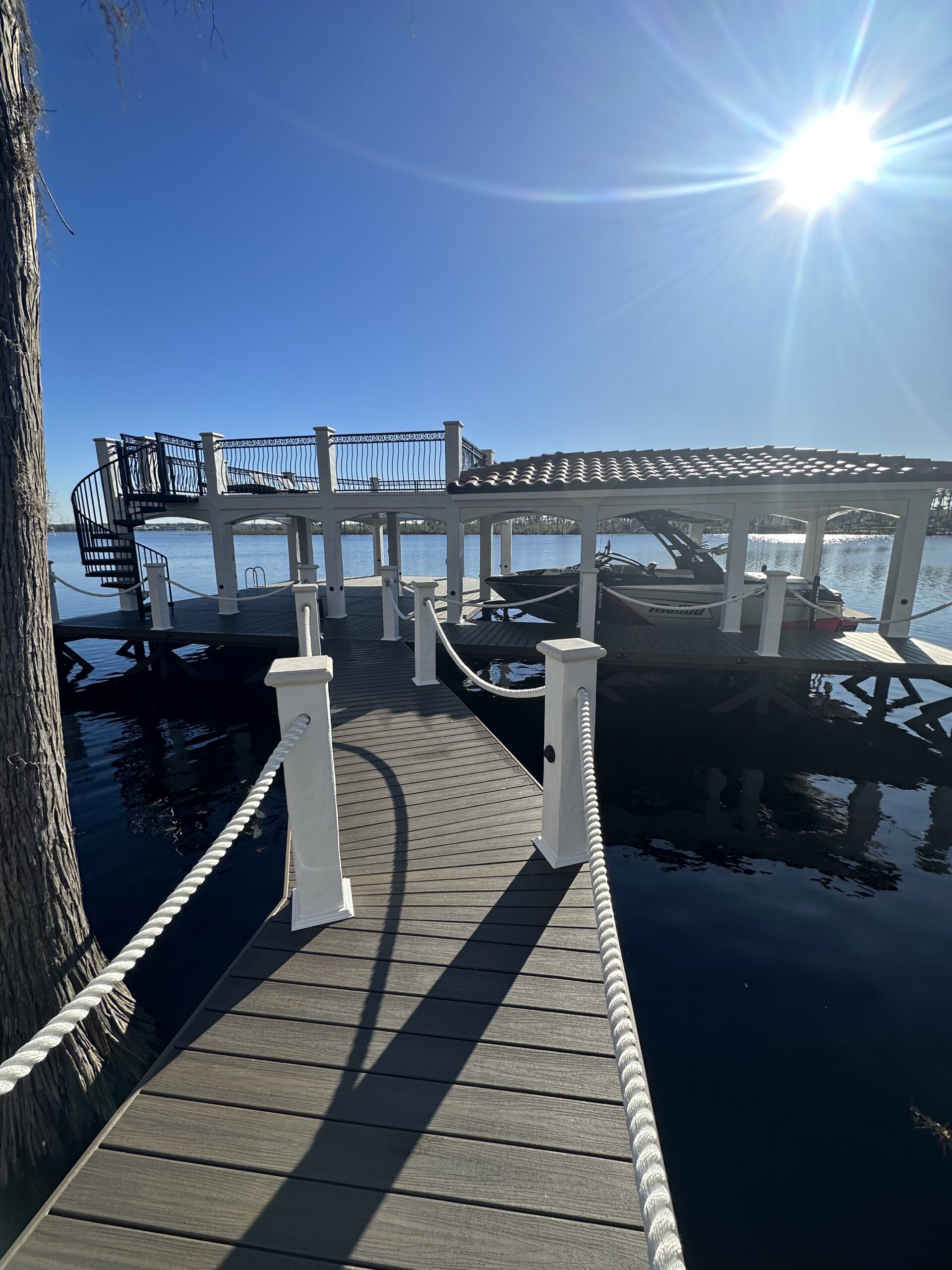 Sunlit dock with white posts and spiral stairway leading to upper platform.