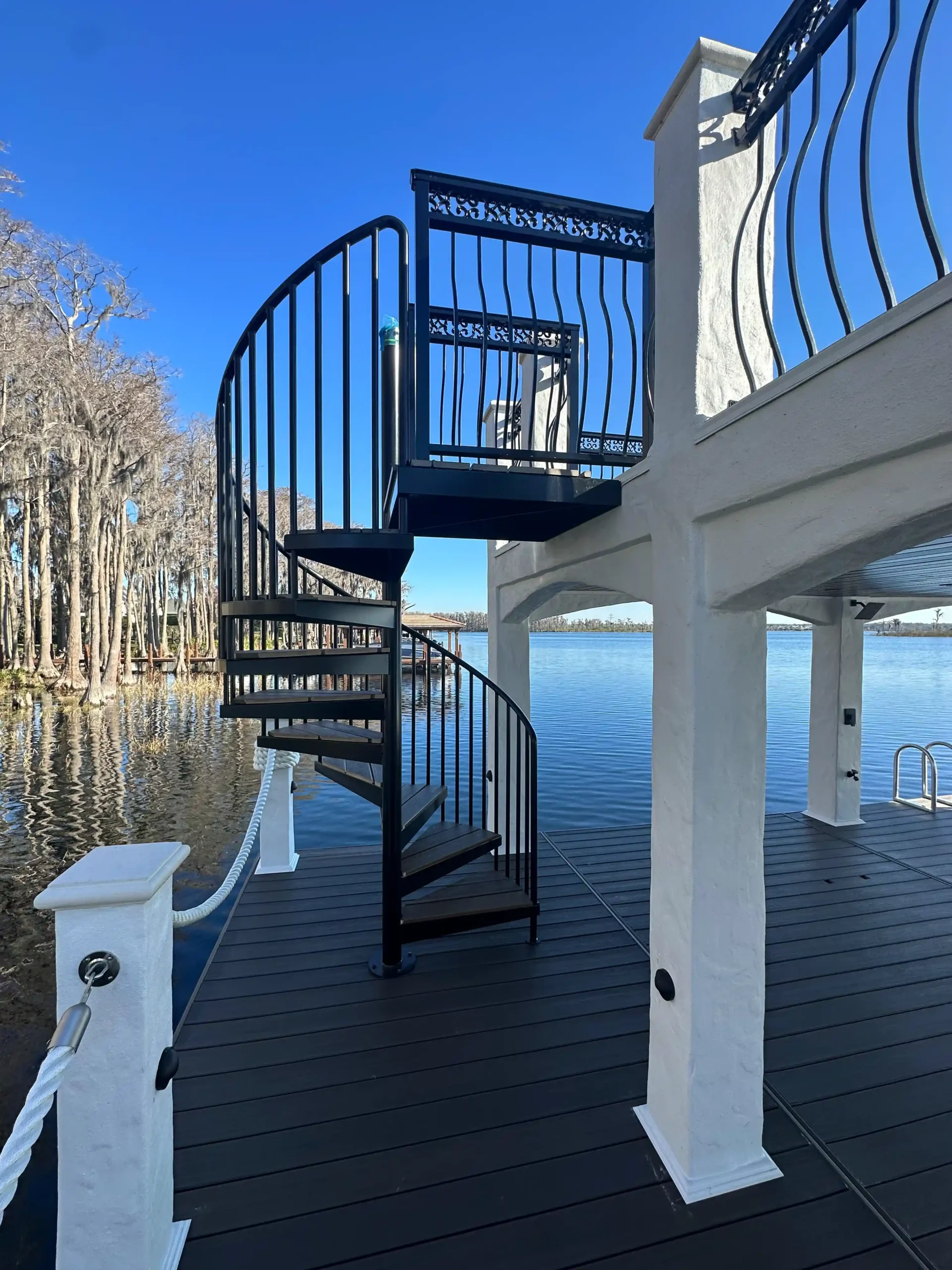 Spiral staircase connecting lower and upper levels of a dock over a lake.