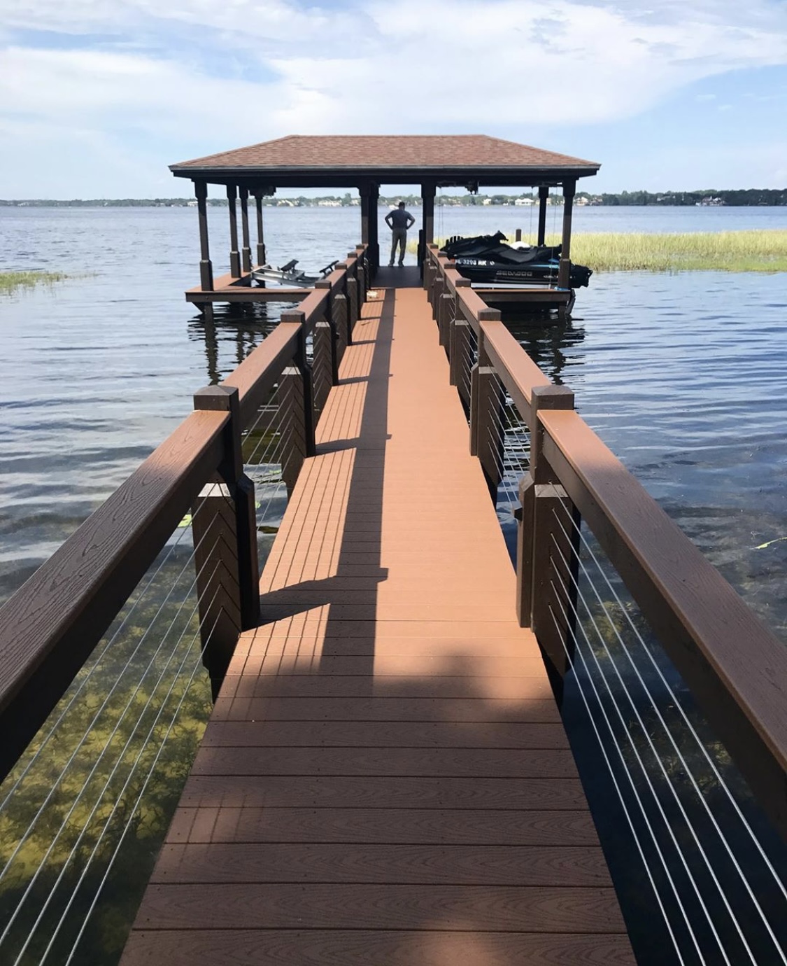 Long wooden pier leading to a covered boat dock on a calm lake under a blue sky.