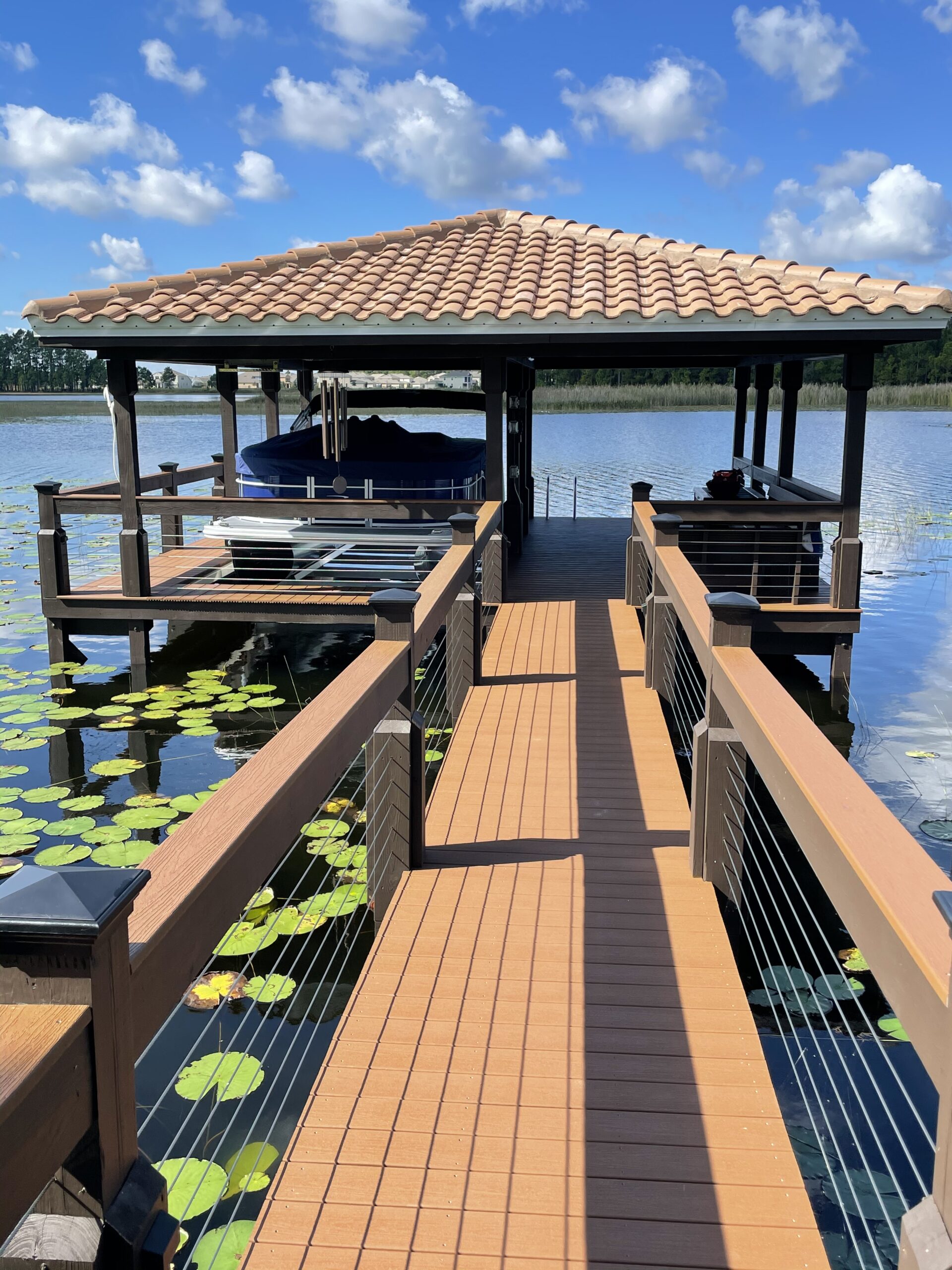 Boat dock with terracotta tile roof and dual boat lifts surrounded by lily pads.