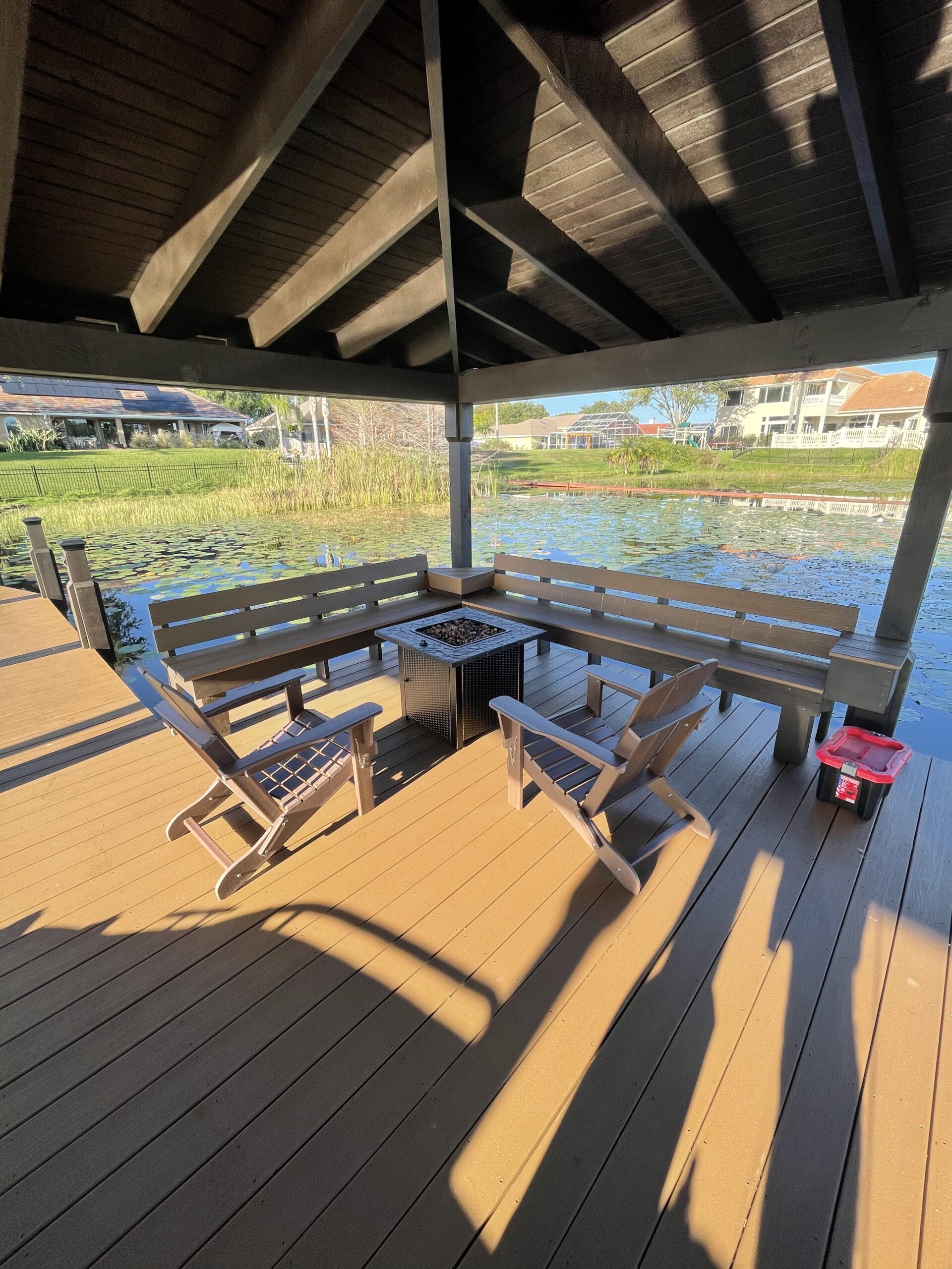 Covered lakeside deck with wooden chairs, built-in benches, and a firepit.